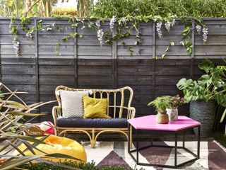 wicker sofa in front of a dark painted garden fence