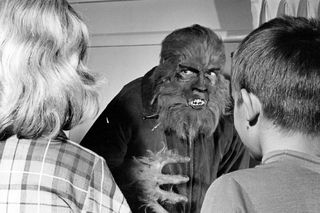Black and white old film image of a werewolf looking at two people.