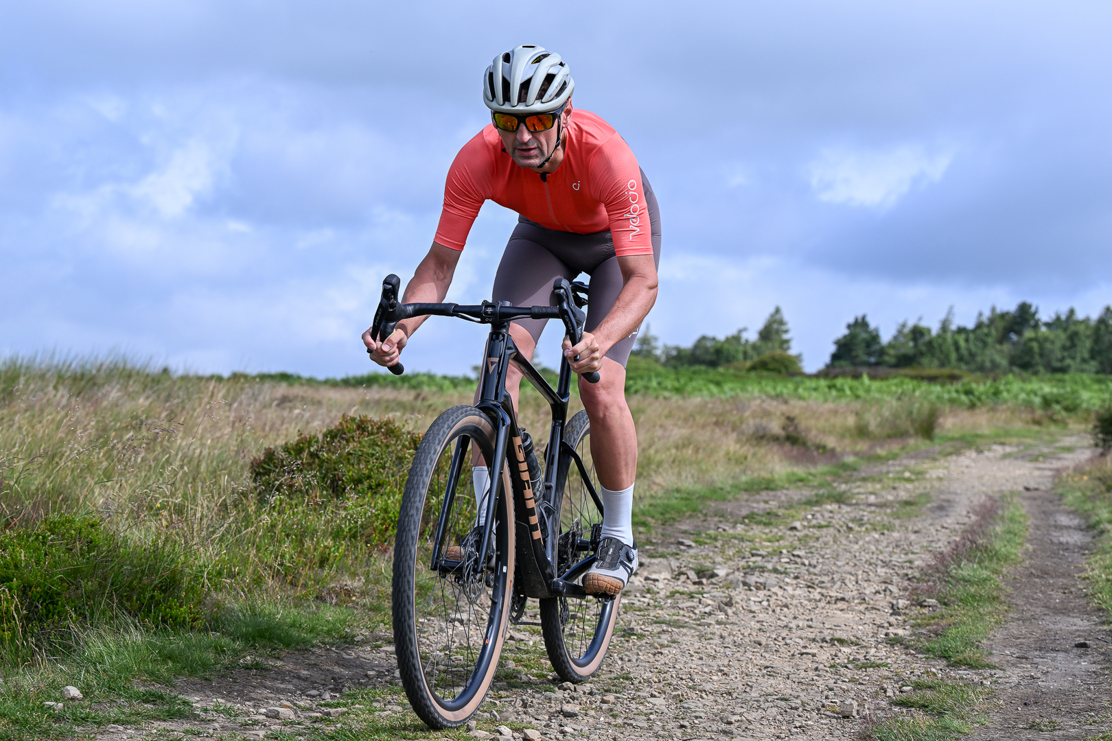 Man in an orange jersey and brown shorts riding downhill towards the camera on a rocky trail