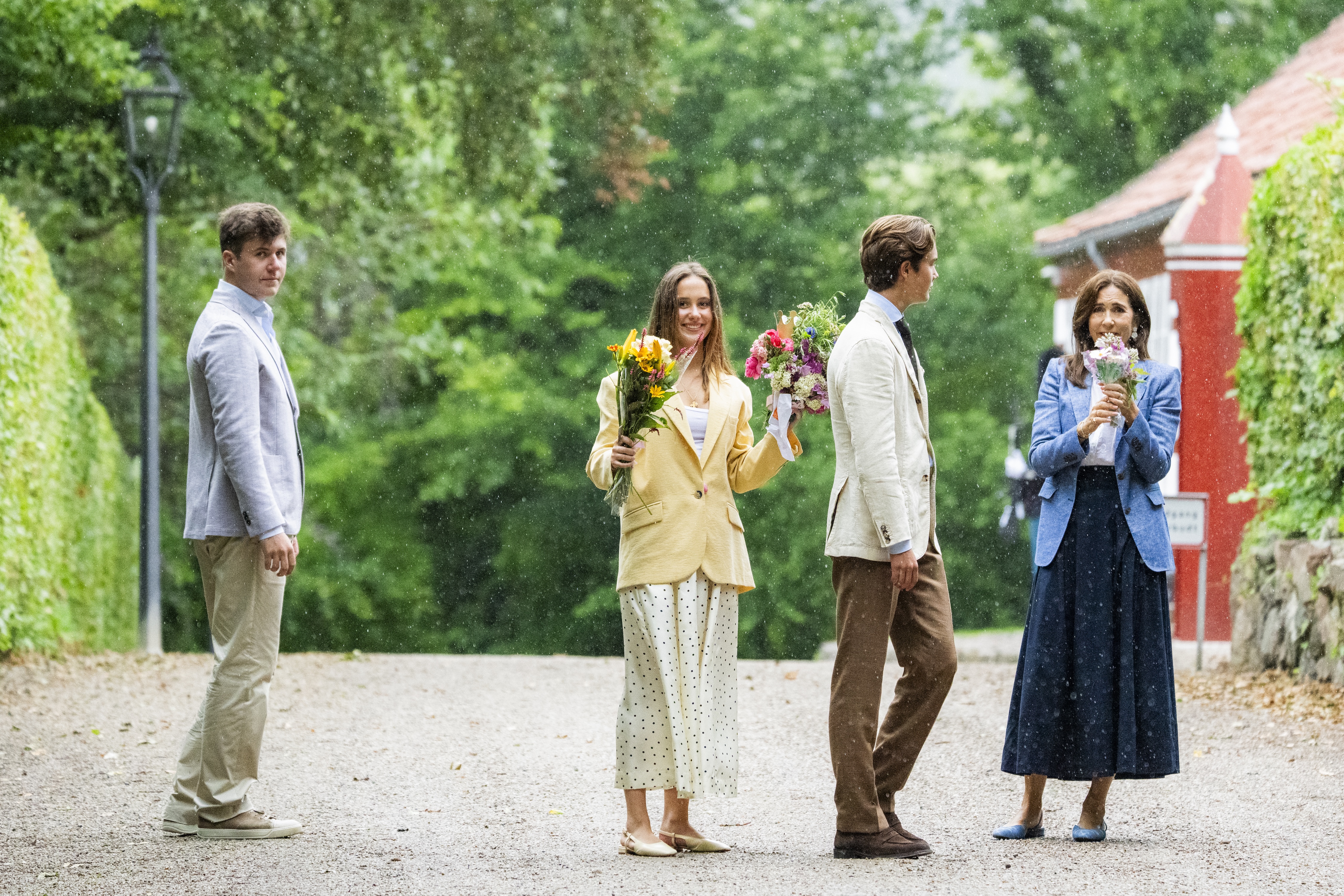 Queen Mary and her kids standing and holding flowers in the rain