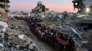 Palestinians gather in the rubble of destroyed buildings to break their fast on the second day of Ramadan in Gaza City