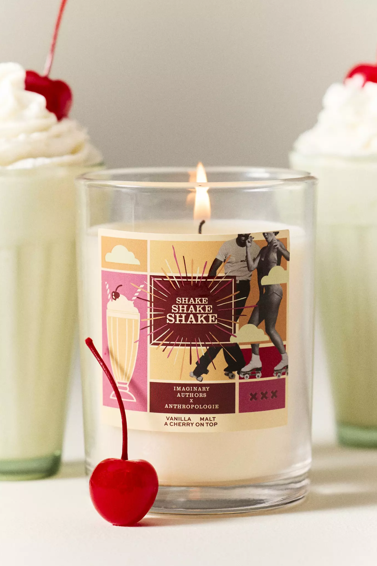 A glass candle by malt milkshakes and red cherries