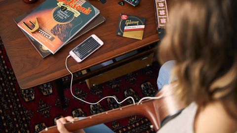 Woman plays an acoustic guitar using the Gibson lessons app