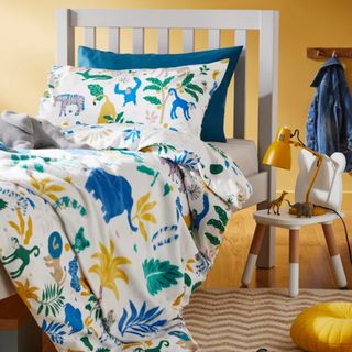 A yellow bedroom with a white wooden bed and a duvet set with a yellow, green and blue animal print