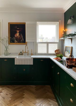 green kitchen with white and green walls, marble worktop, gold tap, shutter and wooden floor