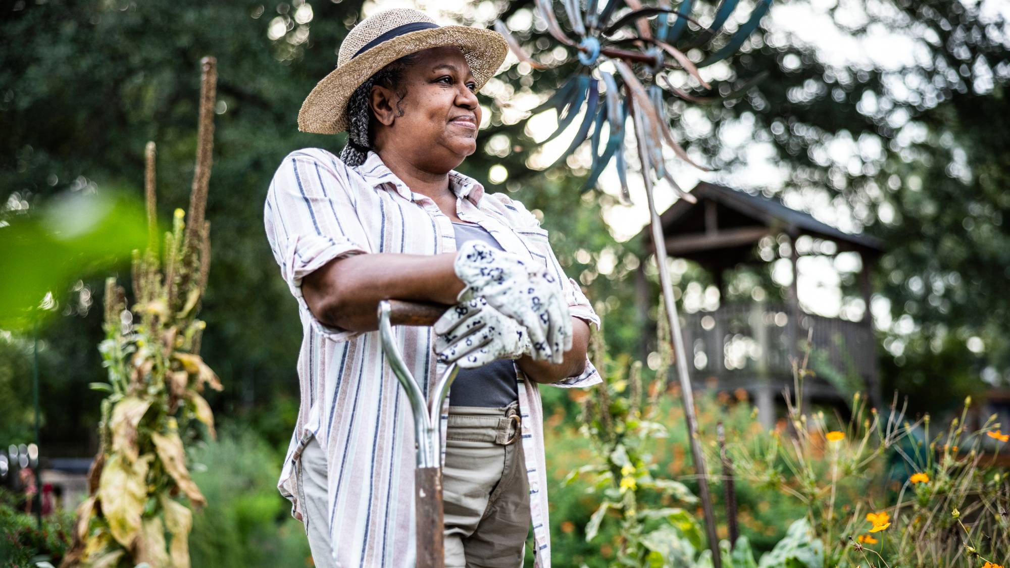 A smiling woman leans on a shovel in a garden