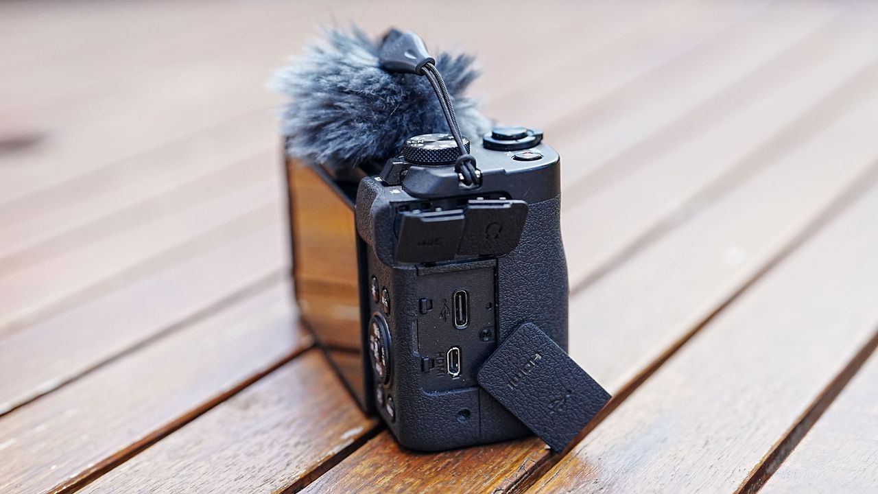 A Canon Powershot V1 on a wooden table with side cover open showing ports.