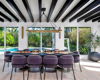 A dining room wall idea with black beams on ceiling, statement lighting and purple chairs