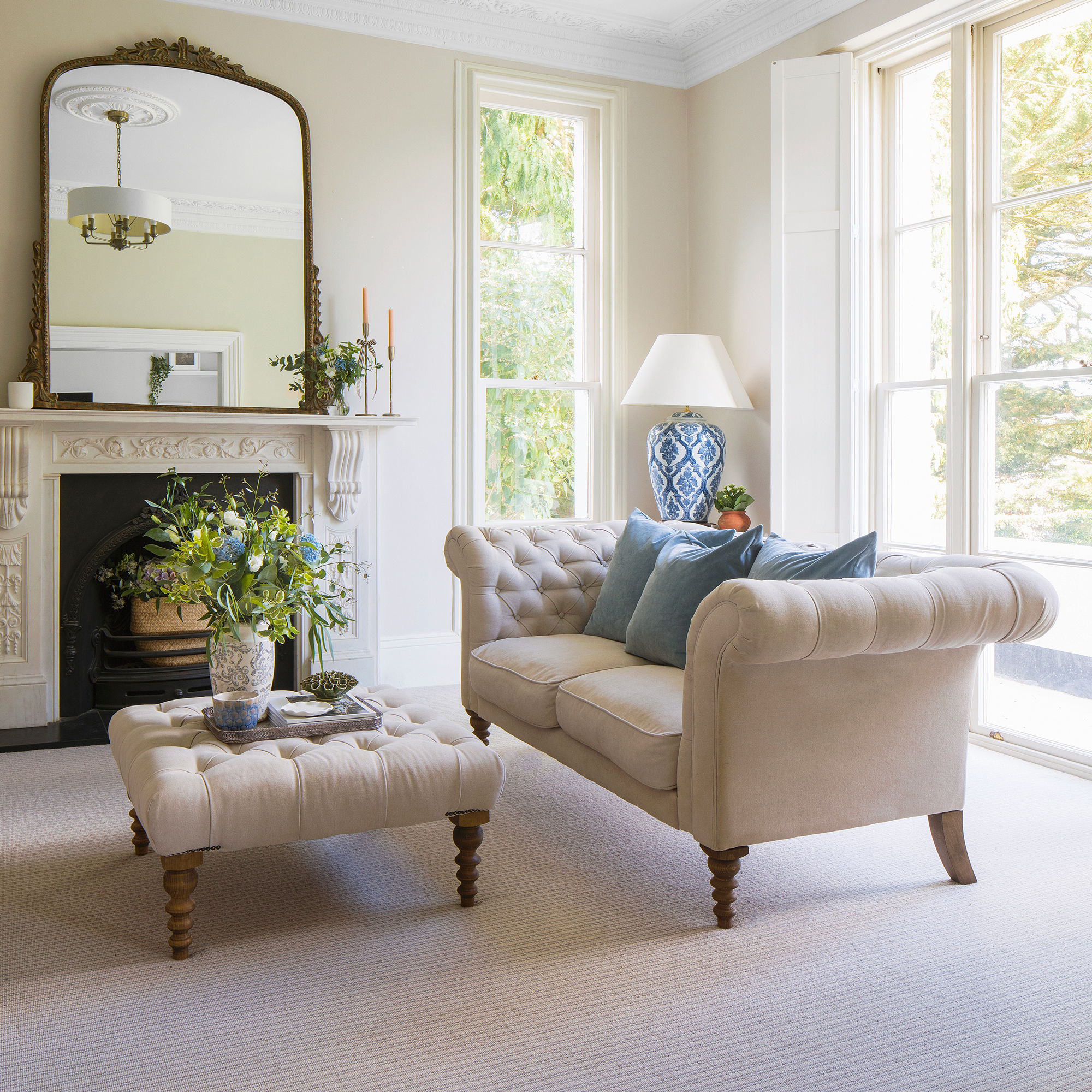 a classic living room with a Chesterfield sofa and matching footstool, dual aspect windows, and a mantelpiece with a large overmantel mirror