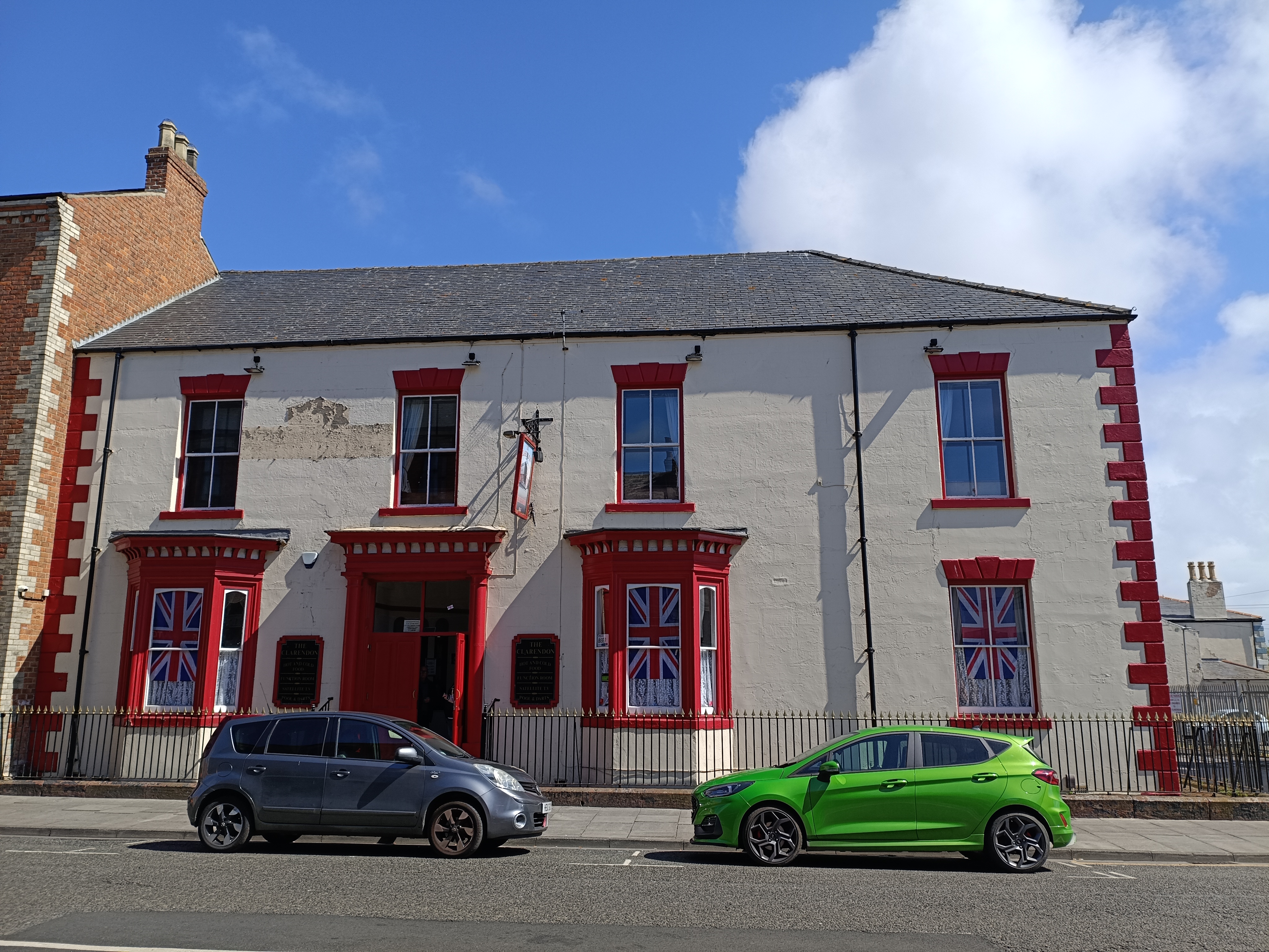 A two-story pub with distinctive red trim around the windows and doors, and two cars parked in front