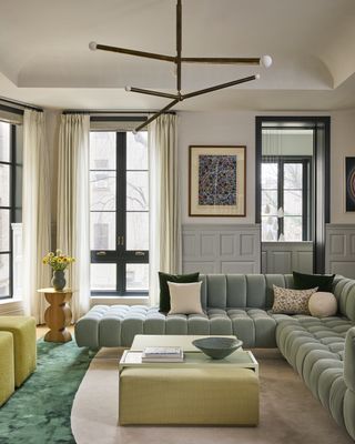 A living room in green tones with a square ottoman in the middle