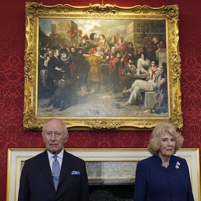 King Charles and Queen Camilla standing in front of a painting on a red wall with serious expressions