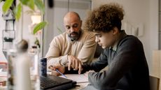 A dad helps his son with financial lessons at the kitchen table.