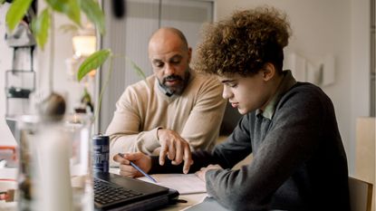 A dad helps his son with financial lessons at the kitchen table.