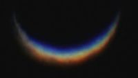 A blurry photo of a crescent shaped rainbow against a black background