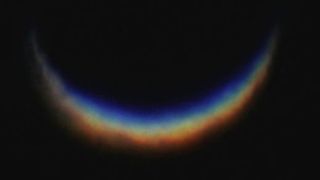 A blurry photo of a crescent shaped rainbow against a black background