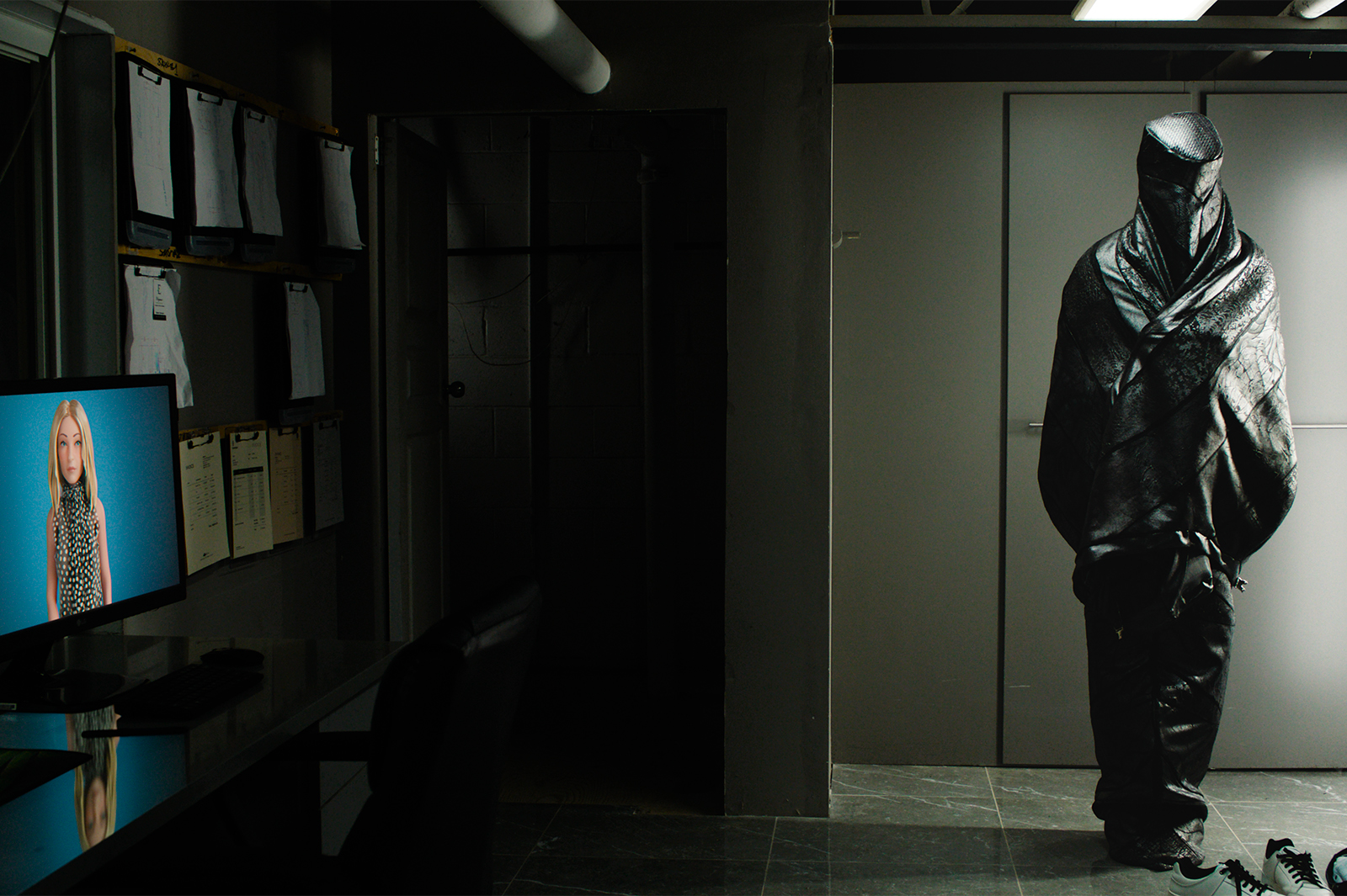 Film still from The Shrouds, showing upright figure in shroud, in darkened room with TV playing