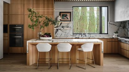 modern timber kitchen with white bar stools, marble backsplash, large window and built-in appliances