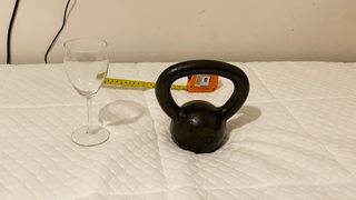 Nectar Essential Hybrid Mattress with a weight resting on it near a wine glass, with a tape measure showing the distance between the two