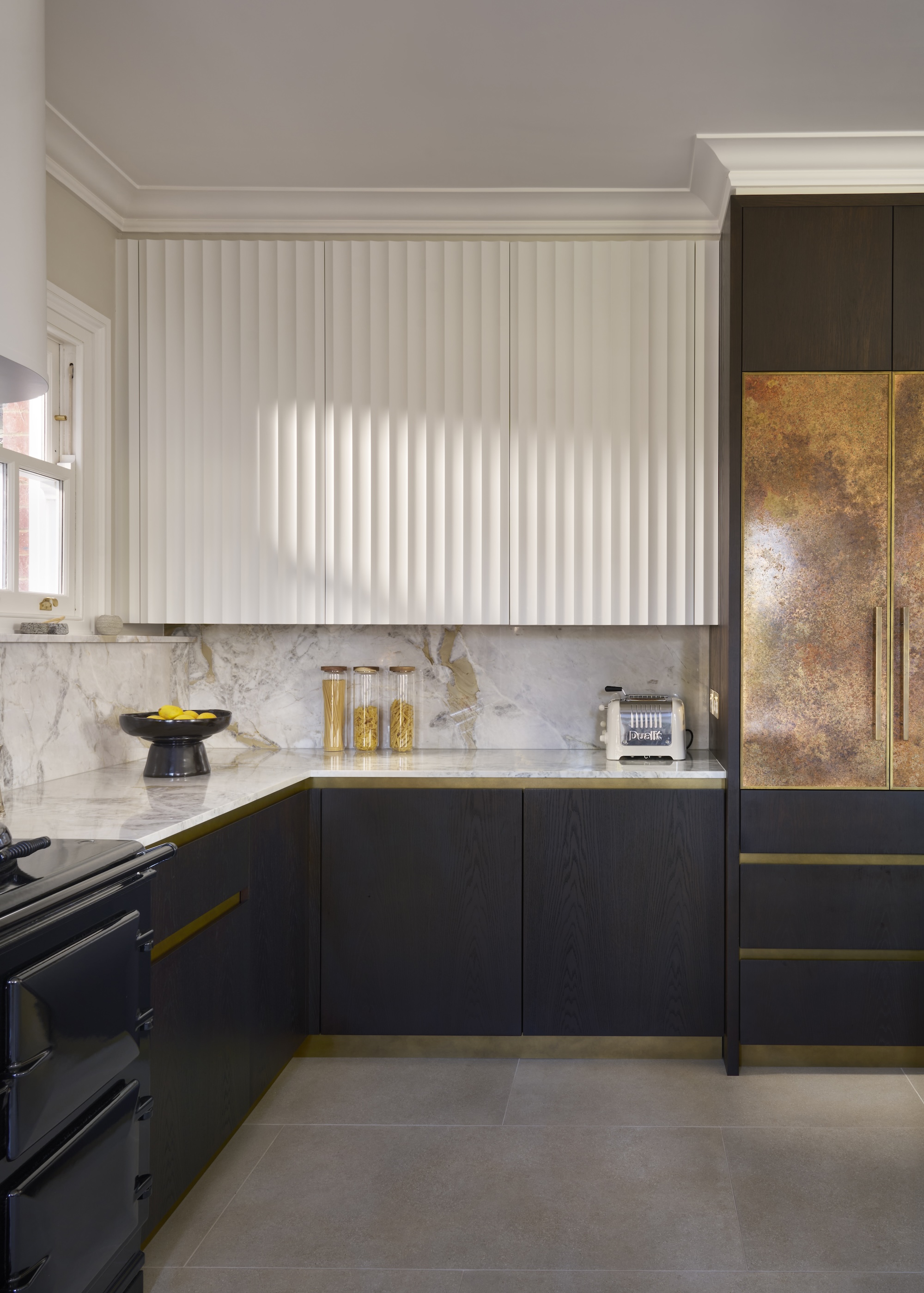 A dark stained kitchen with gold inset handles shown with fluted wall cabinets in painted white shade