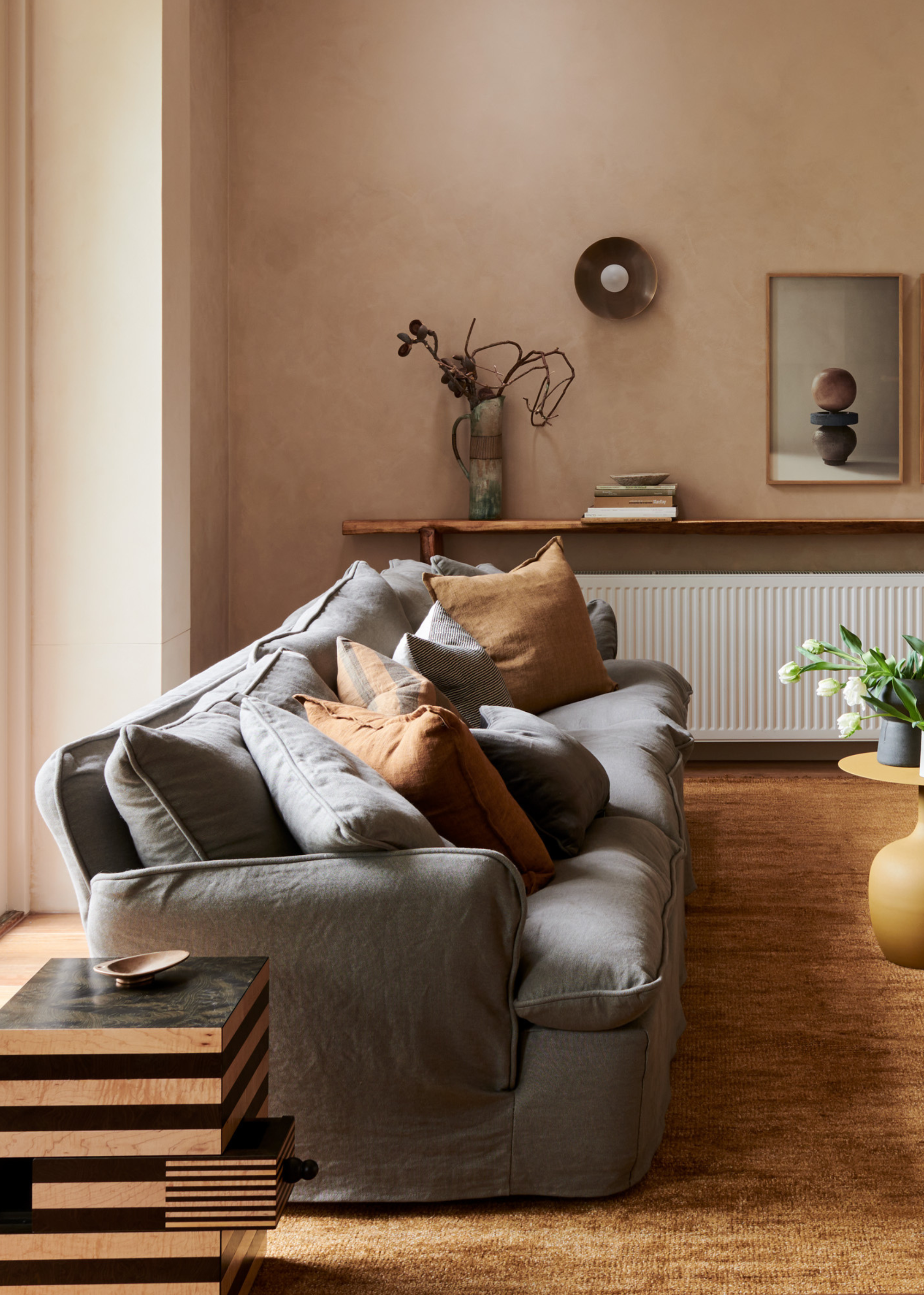 A living room with a blue-gray couch and brown pillows by a stacked dual-tone wood table