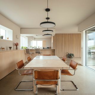 Contemporary kitchen dining space featuring a large wood table and low back red chairs.