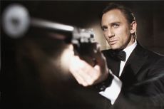 Actor Daniel Craig poses as James Bond, wearing a tuxedo, pointing a gun towards the camera