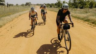 Three gravel riders riding on a dusty gravel road