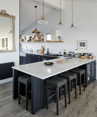 A black kitchen with a breakfast bar and low hanging pendants