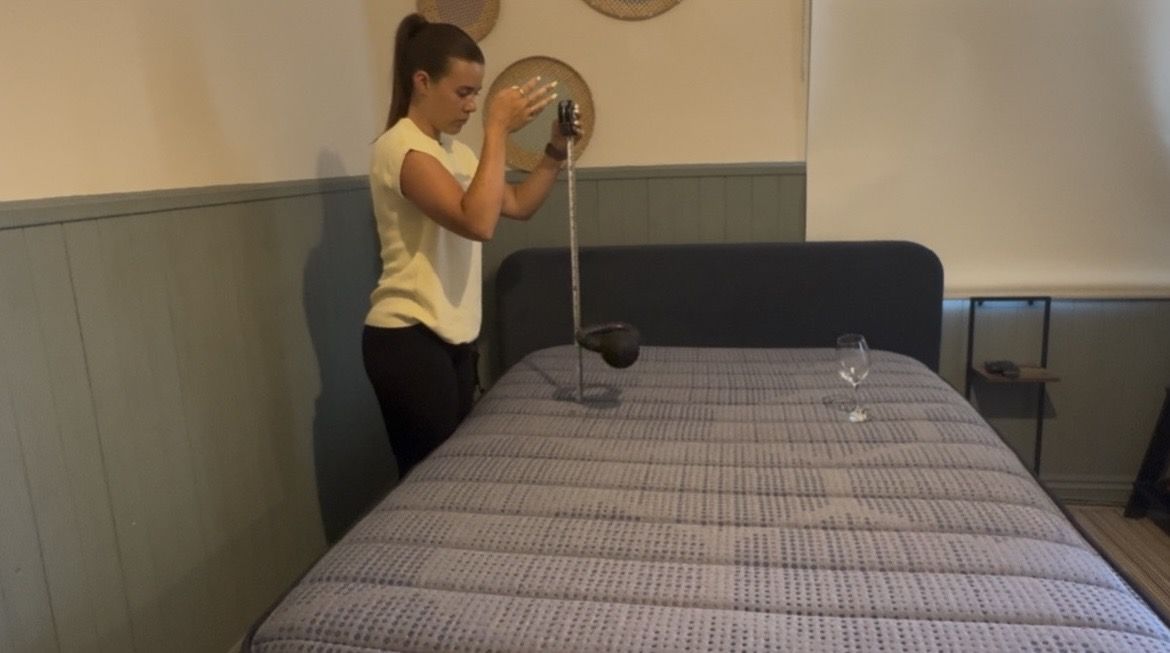 Our mattress tester performing objective motion isolation tests on Brooklyn Bedding Copperflex Memory Foam Mattress. Wearing a yellow top, she drops a kettlebell on to the left hand side of the bed with a wine glass standing on the other side.