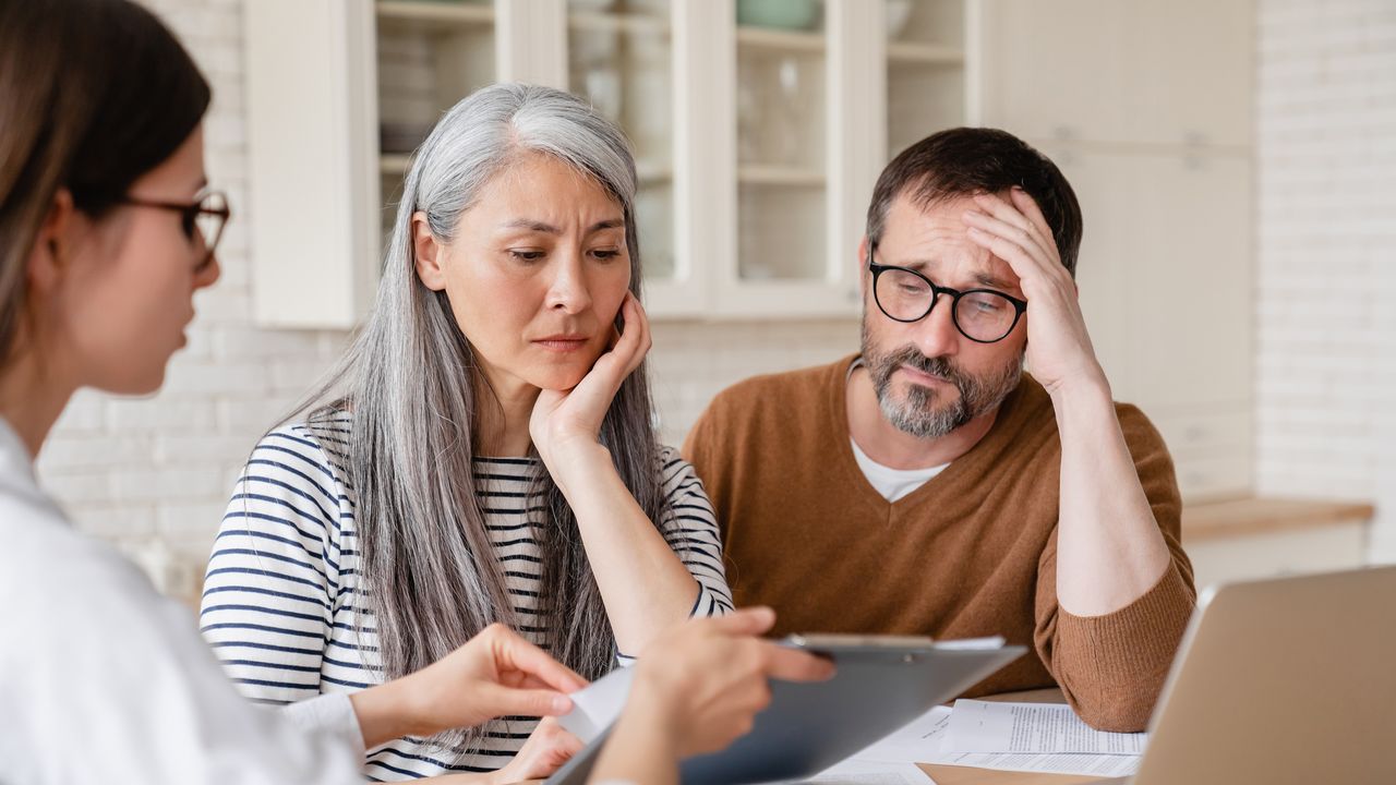 A couple look worried as they look at a tablet their financial adviser is showing them.