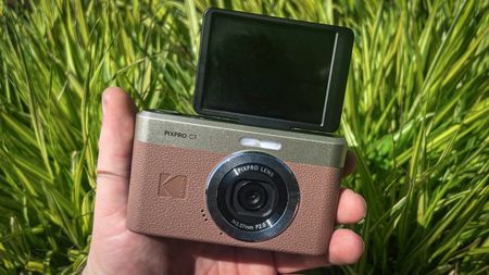 Kodak Pixpro C1 being held in one hand in front of green rush-like plant