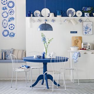 white panelled kitchen with blue dining table, chairs, bank of cushioned seating and rich blue wall