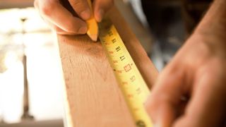 Person measuring and marking wood with a pencil 