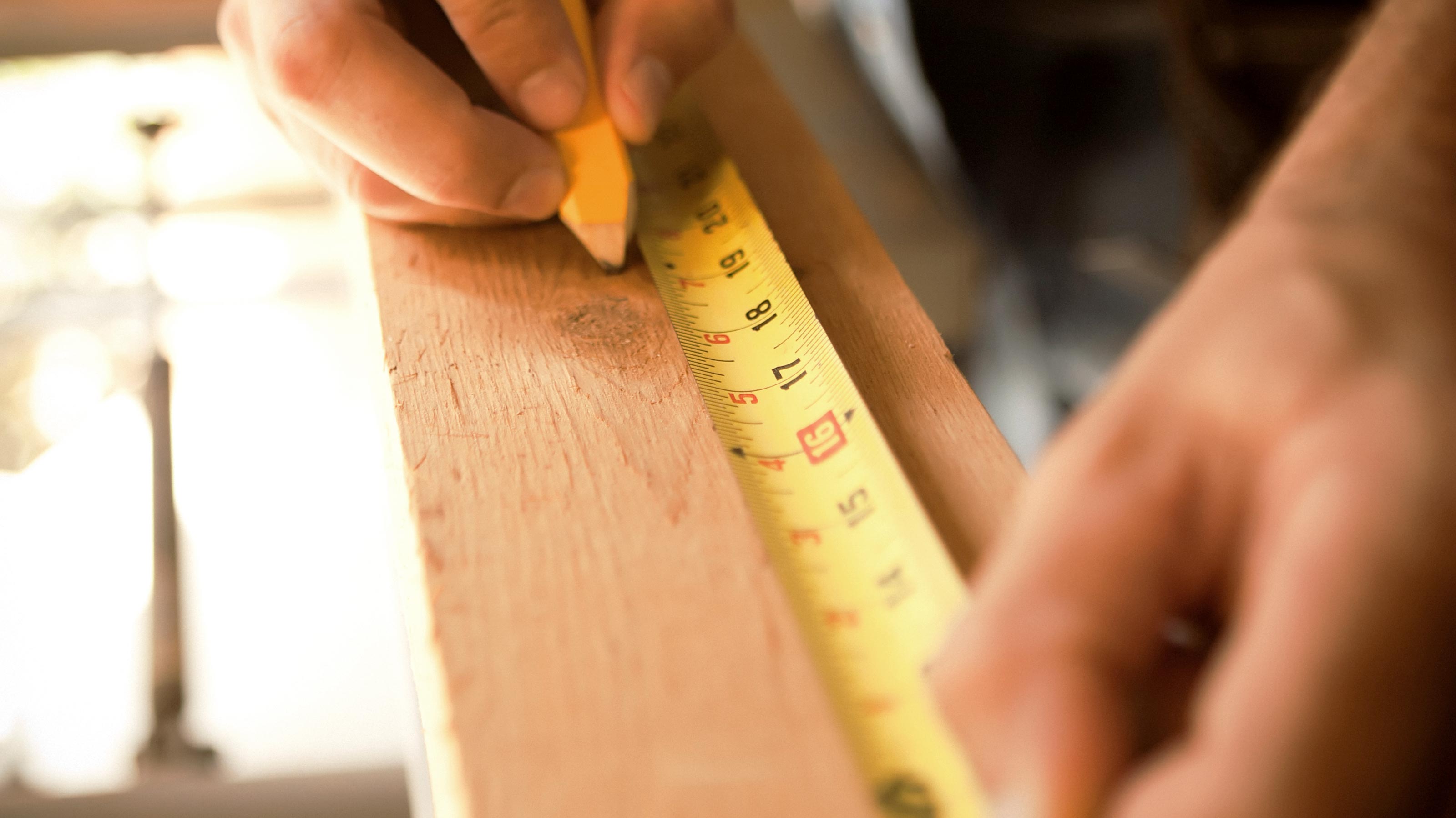 Person measuring and marking wood with a pencil