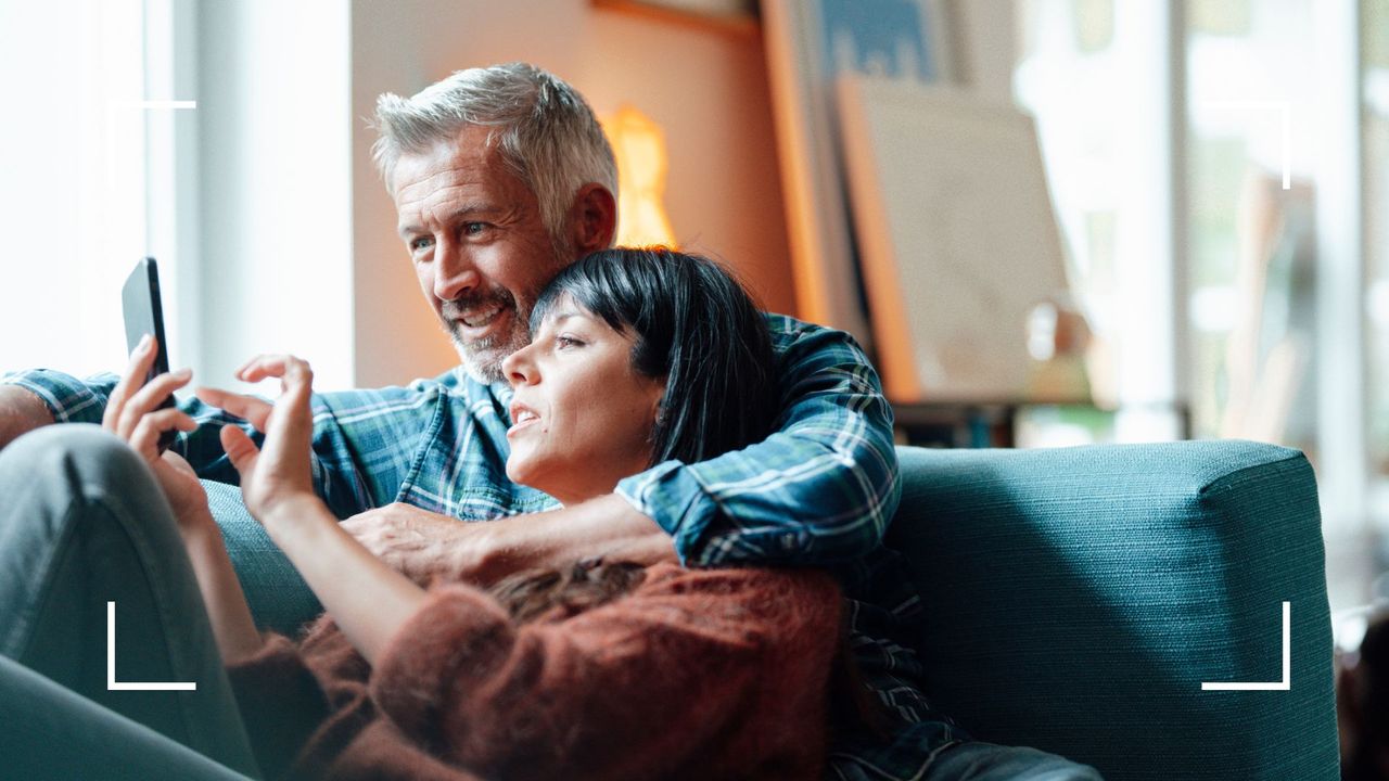 Couple lying together on the sofa at home looking at mobile phone, representing low libido in menopause