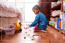 A young boy sat on the floor while putting toys into boxes