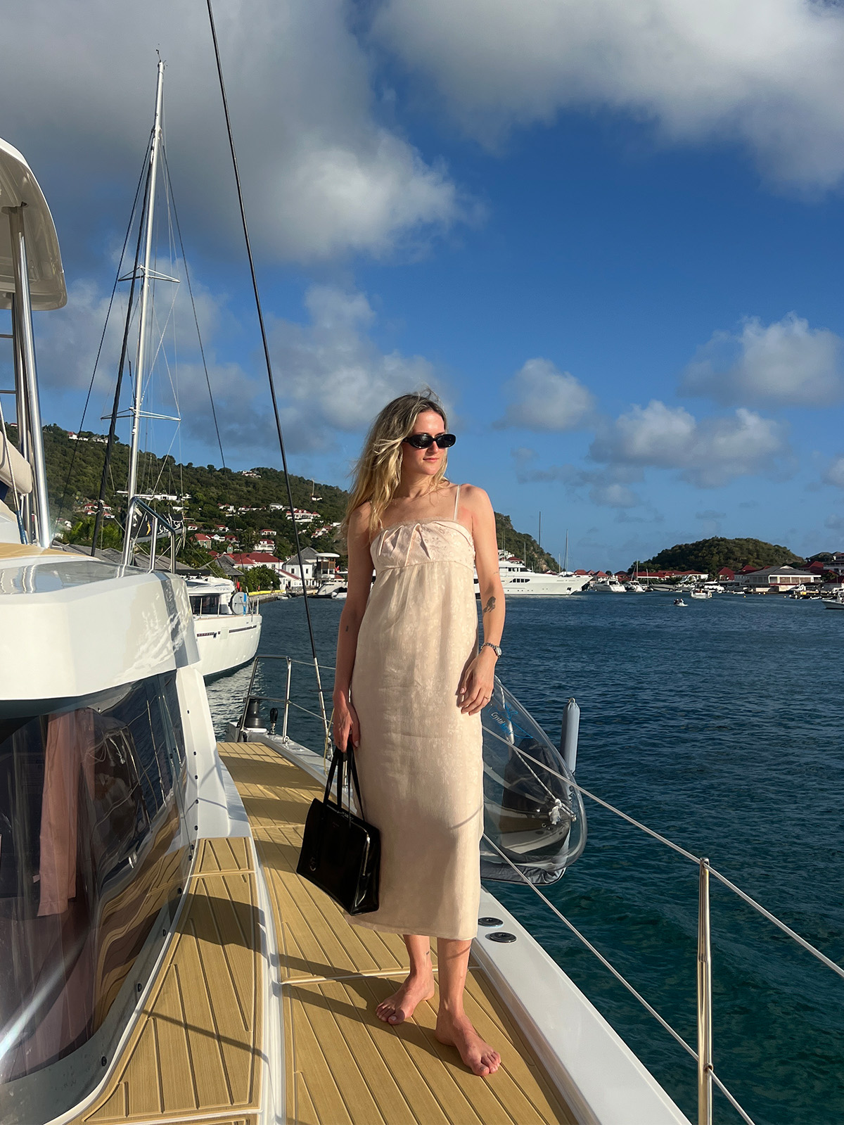 Eliza Huber wearing a pink Zara midi dress on a boat with a black Prada bag and black sunglasses.
