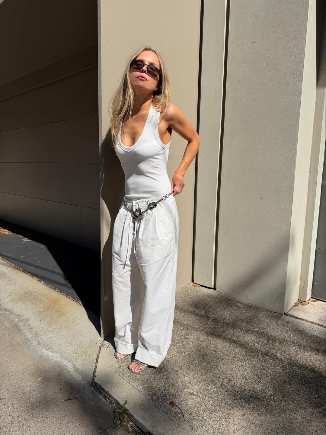 Influencer Rachelle Rowlings wearing a white vest top, wide-leg trousers, chain belt and heeled sandals.