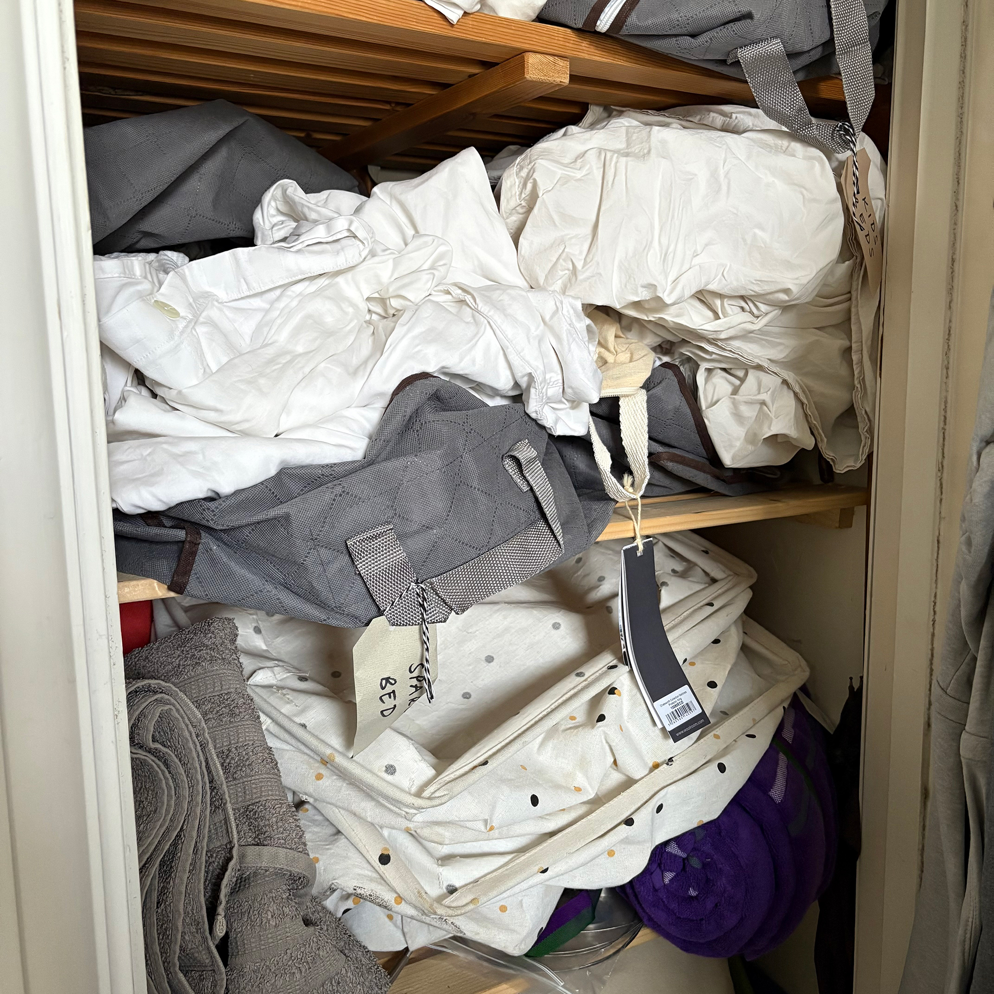 Airing cupboard with messy bedding and storage bags and baskets