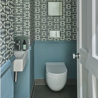 downstairs toilet with white wall hung toilet, white basin, grey and white patterned wallpaper above blue wall paint