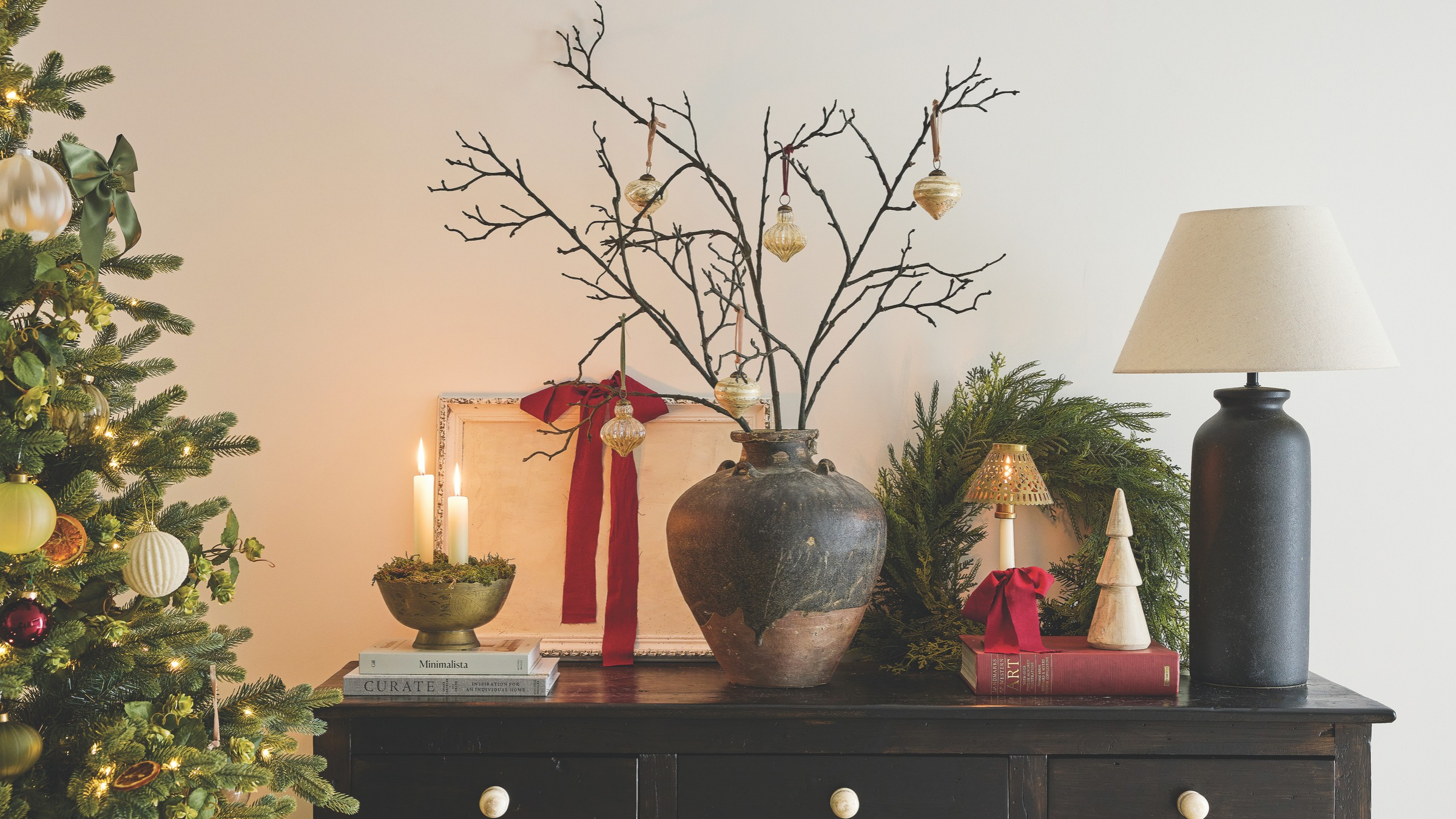 Dresser decorated with lamp, wreath, cnaldes and vase with foliage and baubles.