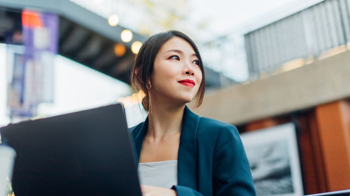 A businesswoman is sitting at her laptop while looking off to the side and smiling