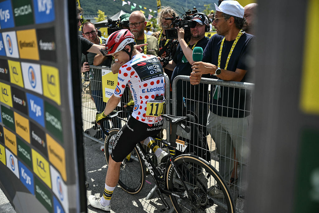 Accredited media members line a barrier to conduct interviews, as Team Visma - Lease a bike team's Danish rider Jonas Vingegaar wearing the best climber's polka dot (dotted) jersey awaits the start of the 19th stage of the 112th edition of the Tour de France cycling race, 93.1 km between Albertville and La Plagne, in the French Alps, on July 25, 2025. The 19th stage of the Tour de France was shorted from its initial 129.9 km route, bypassing the Col des Saisies where an outbreak of nodular dermatitis in a herd of cattle was discovered, prompting organizers to modify the race route. (Photo by Marco BERTORELLO / AFP)