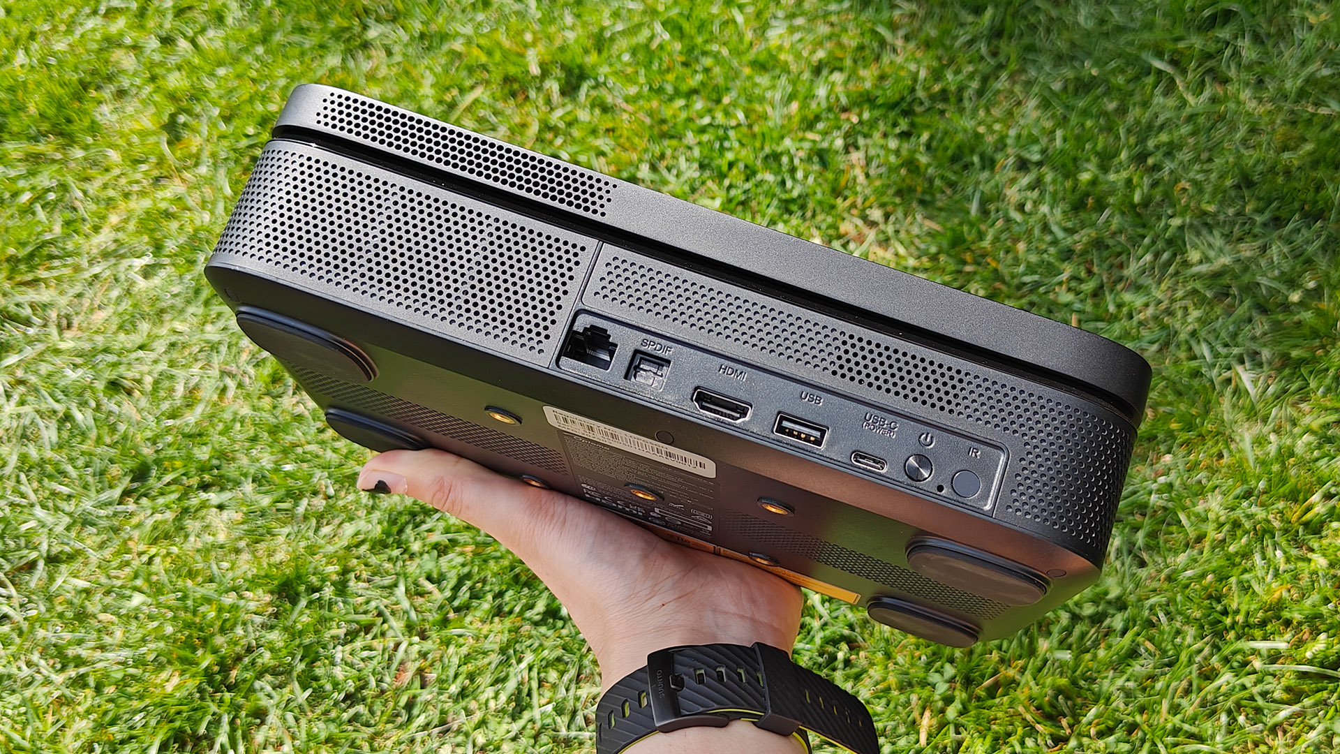 Optoma Photon Go portable UST projector held in hand over grassy lawn showing rear connections