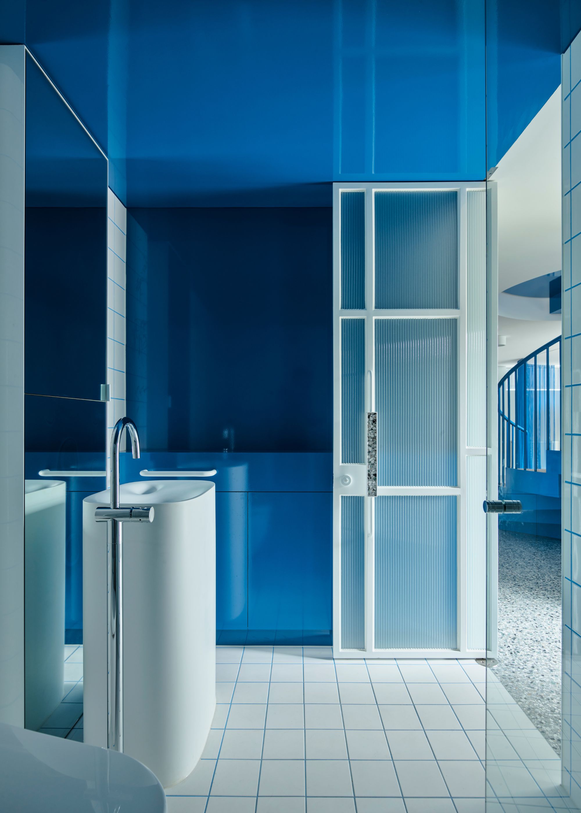 A bathroom with blue reflective walls, and tiles in white with blue grout