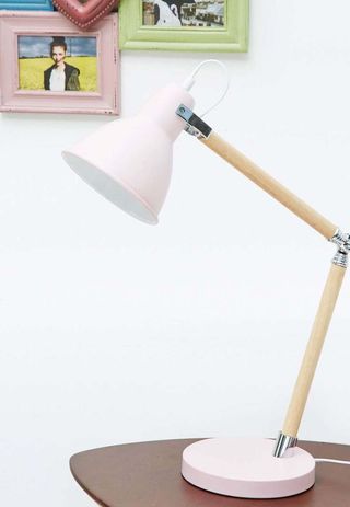 Pink Table Lamp with wooden arms, sitting on a desk with photographs displayed on the white wall in the background