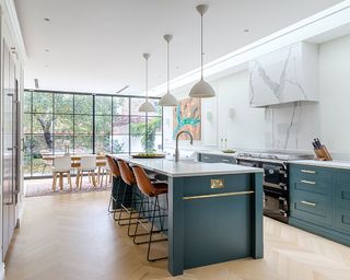 A large kitchen extension with dark green cabinets and an island with leather bar stools and a built in sink below pendant lighting