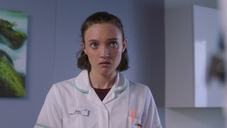 Amy Darton as student midwife Vicky in a white uniform with pale green trim looking like she's in toruble.