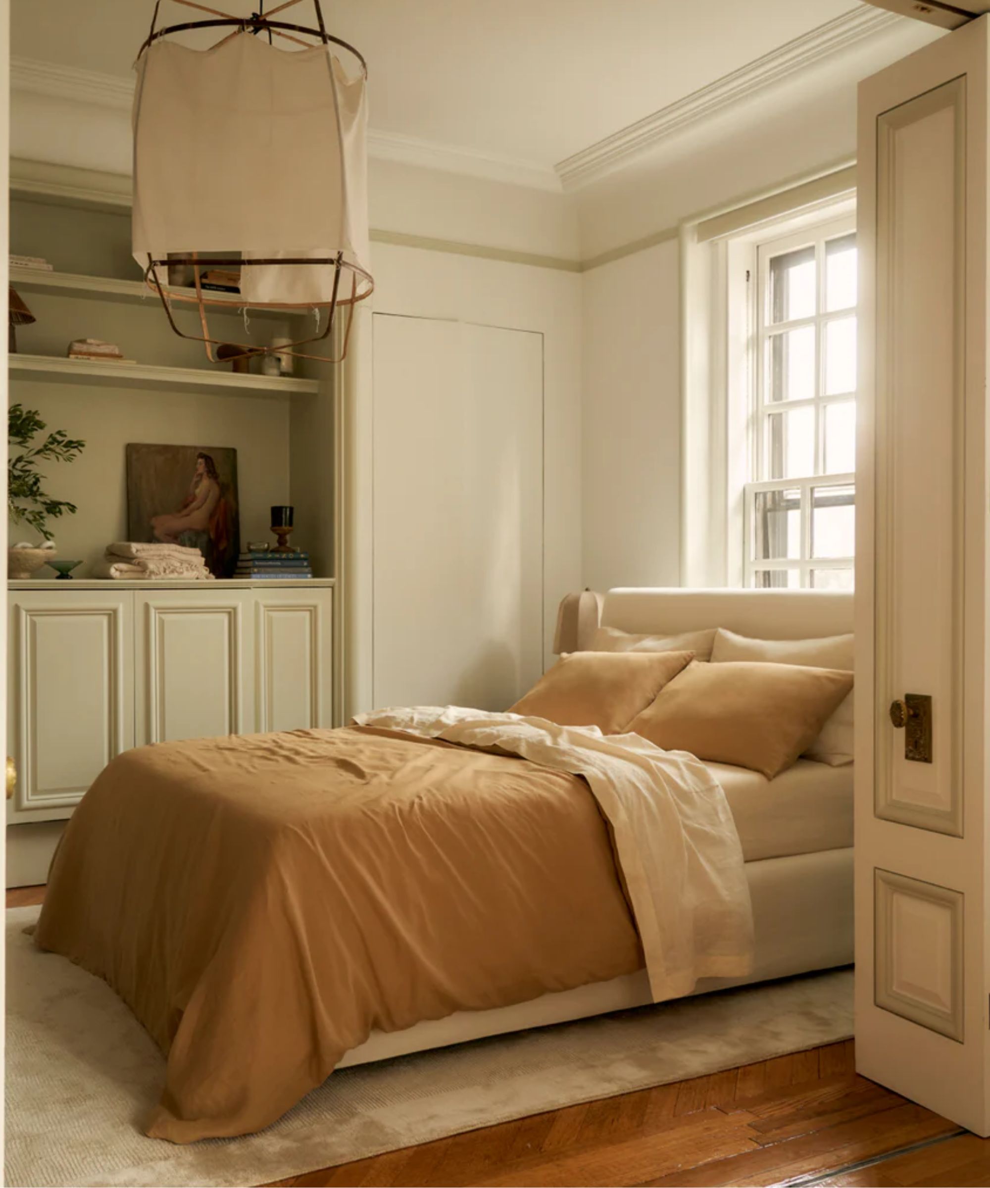 traditional bedroom space with large ornate doors leading into the space, wooden floor, a rug, and a neutral bed with caramel bed linen
